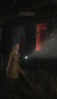 woman in brown coat standing near white house during night time