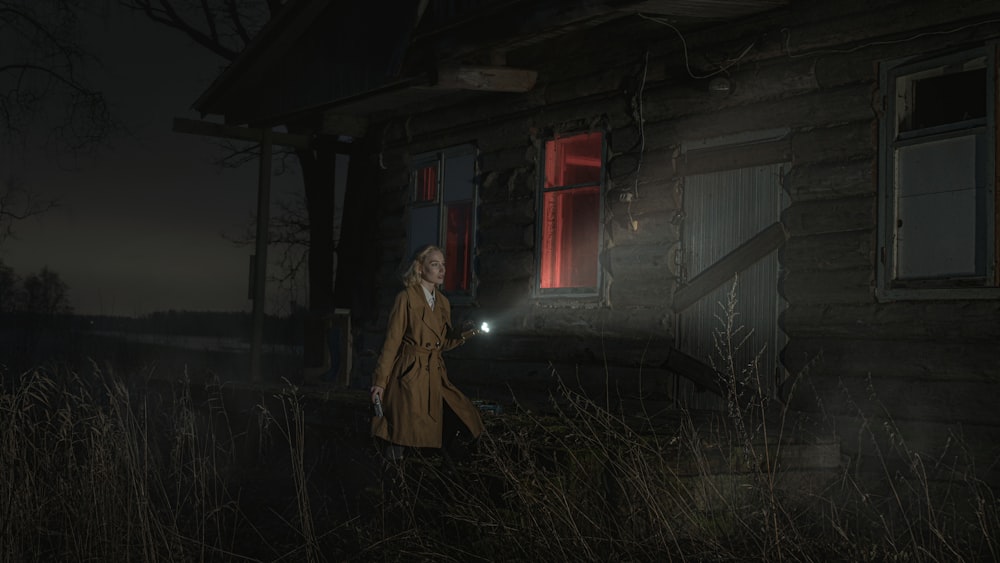 woman in brown coat standing near white house during night time