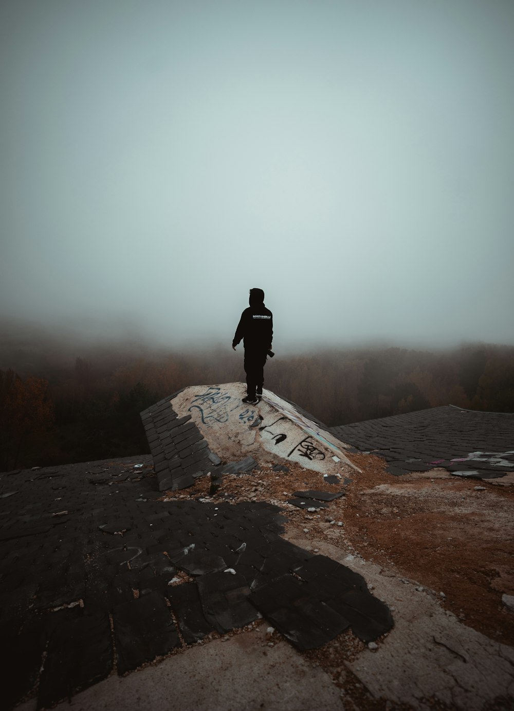 man in black jacket standing on gray concrete bench during daytime