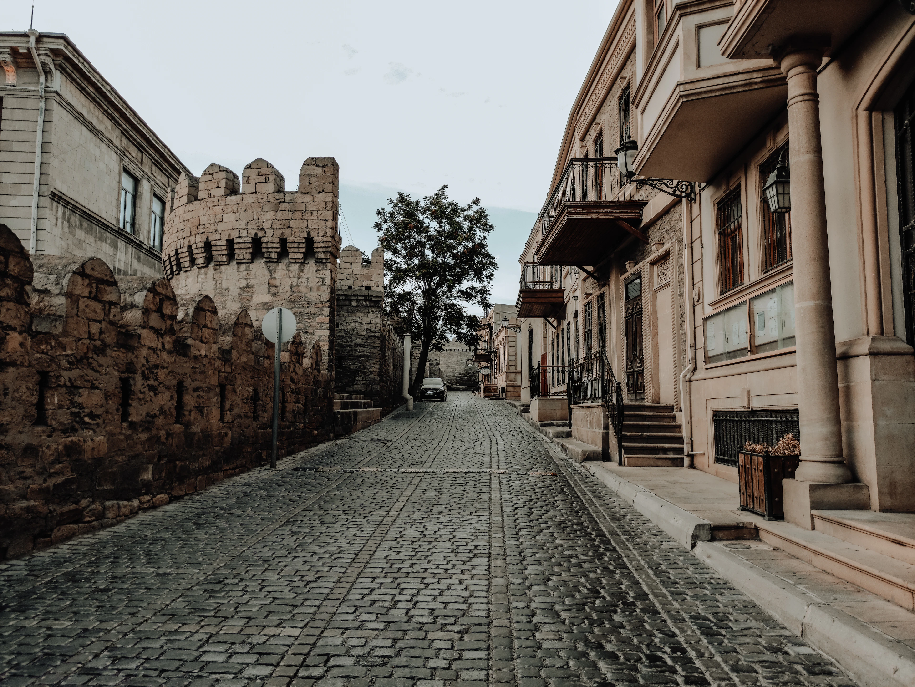 A cobbled lane inside Baku's walled Old City, with the medieval fortress wall on one side and stone townhouses on the other