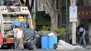 Team members carrying boxes and junk items towards a hauling truck on a sunny day.