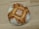 A round, rustic loaf of bread with a crusty, golden-brown exterior and a dusting of flour on top. The pattern on the bread suggests a traditional baking method, and it is resting on a light wooden surface.