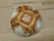 A round, rustic loaf of bread with a crusty, golden-brown exterior and a dusting of flour on top. The pattern on the bread suggests a traditional baking method, and it is resting on a light wooden surface.