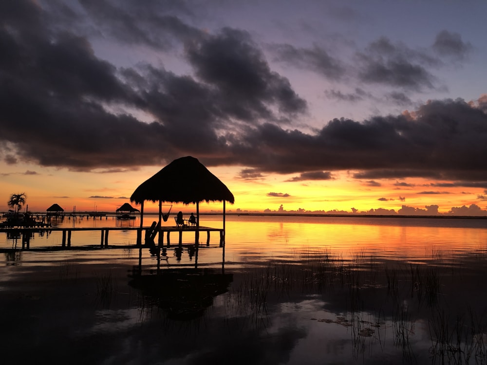 brown wooden beach house on body of water during sunset