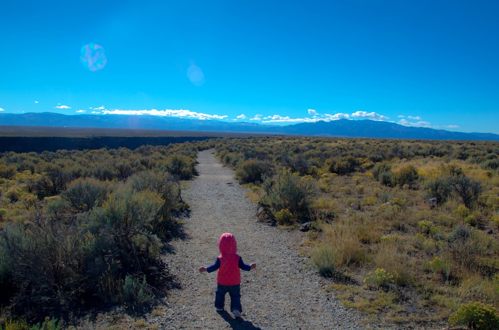 person in black jacket walking on dirt road during daytime