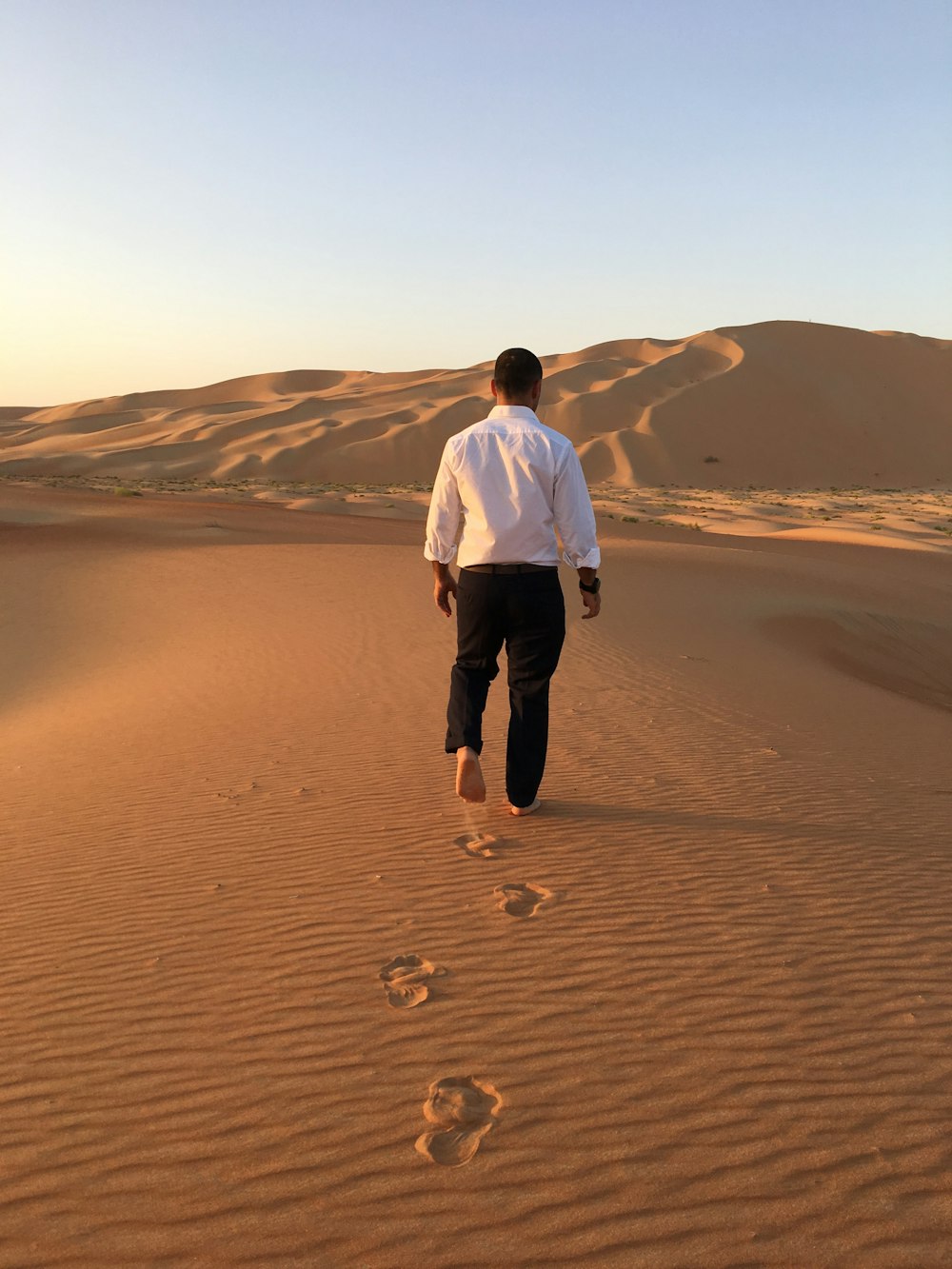 man in white dress shirt and black pants standing on brown sand during daytime