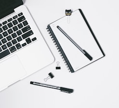 Minimalist workspace with a notebook, pen, and turquoise accent details on a white desk.