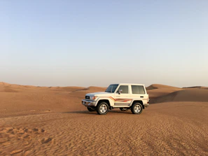 A sleek white SUV parked on a sandy desert road under a clear blue sky