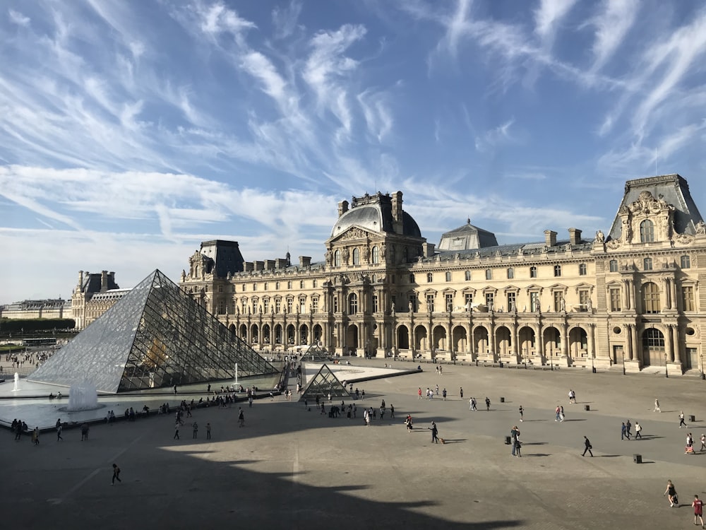 personnes marchant sur une route en béton gris près d’un bâtiment en béton brun sous un ciel nuageux bleu et blanc