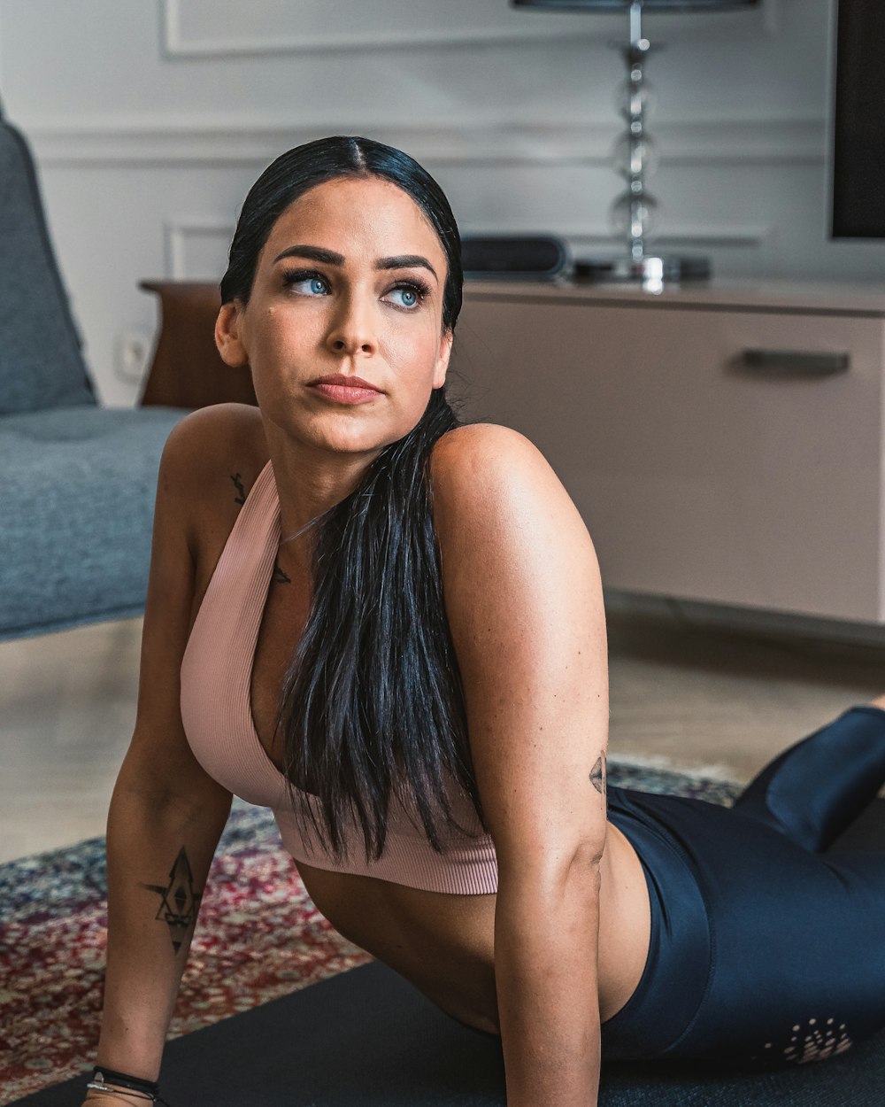 woman in blue tank top and black leggings lying on blue and white floral area rug