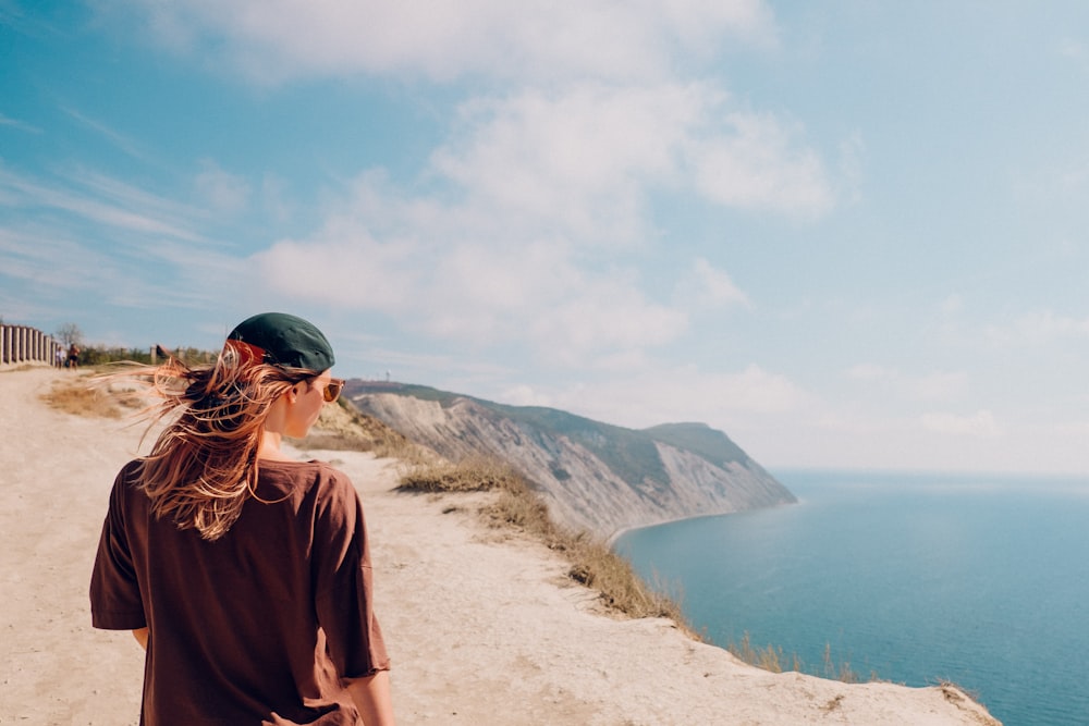 woman in brown shirt standing on brown field near body of water during daytime