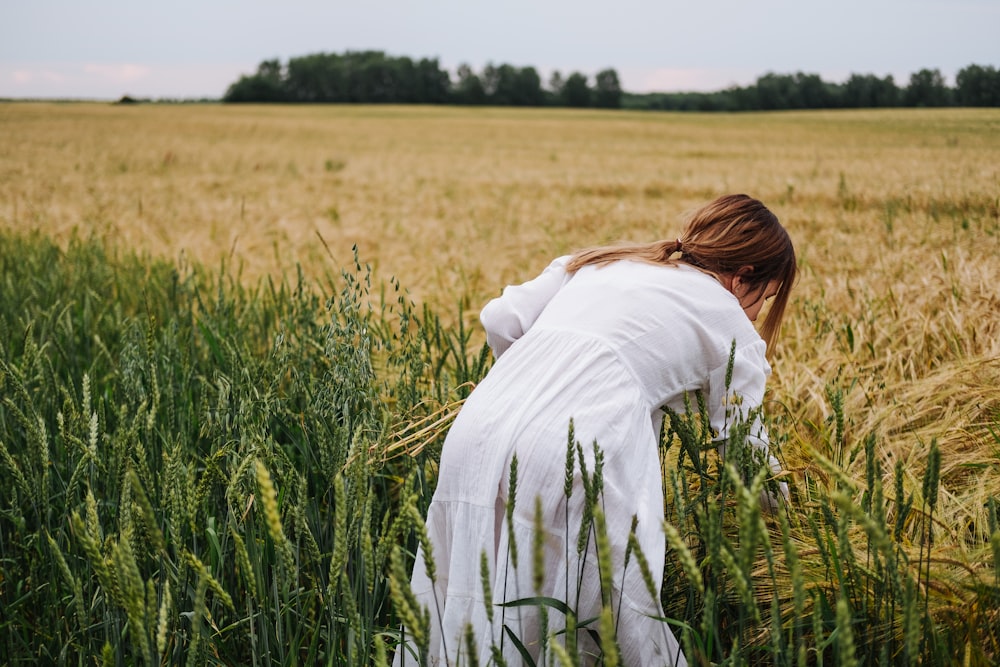 mulher na camisa branca da manga comprida que está de pé no campo verde da grama durante o dia