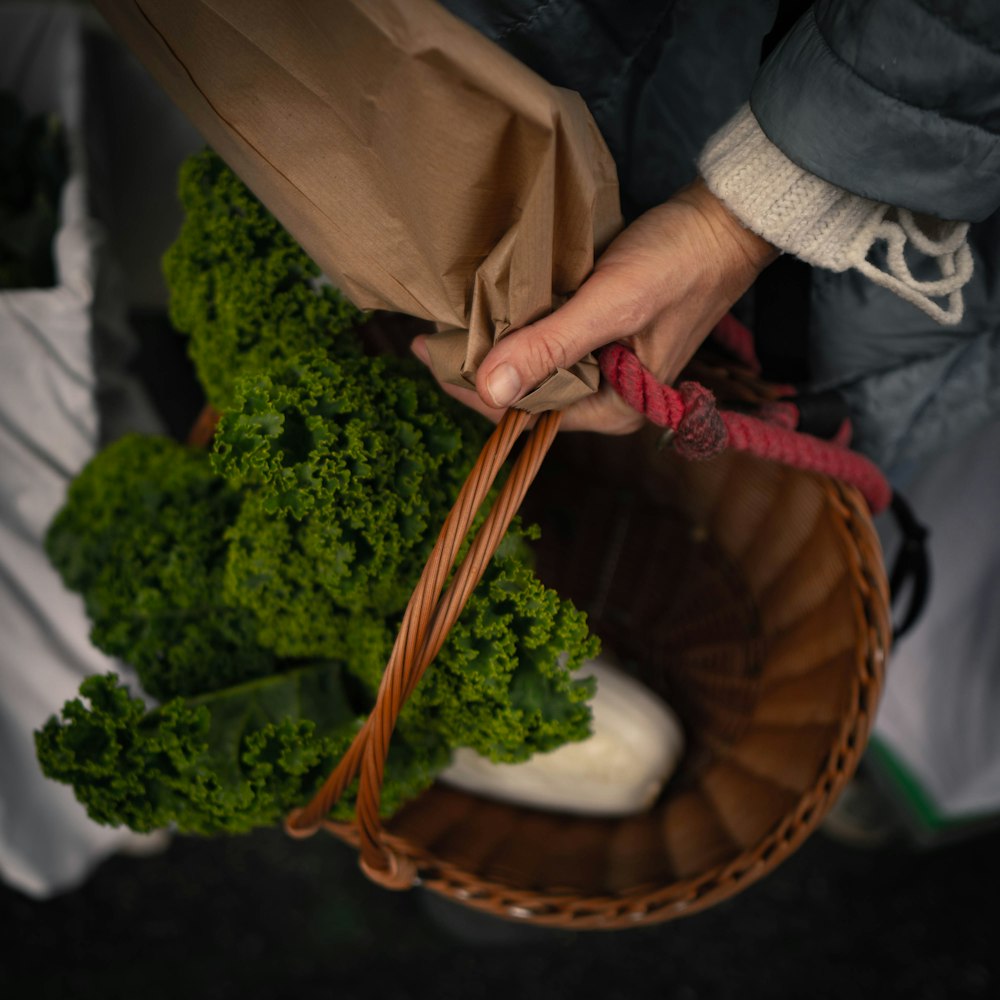 a person holding a basket full of broccoli