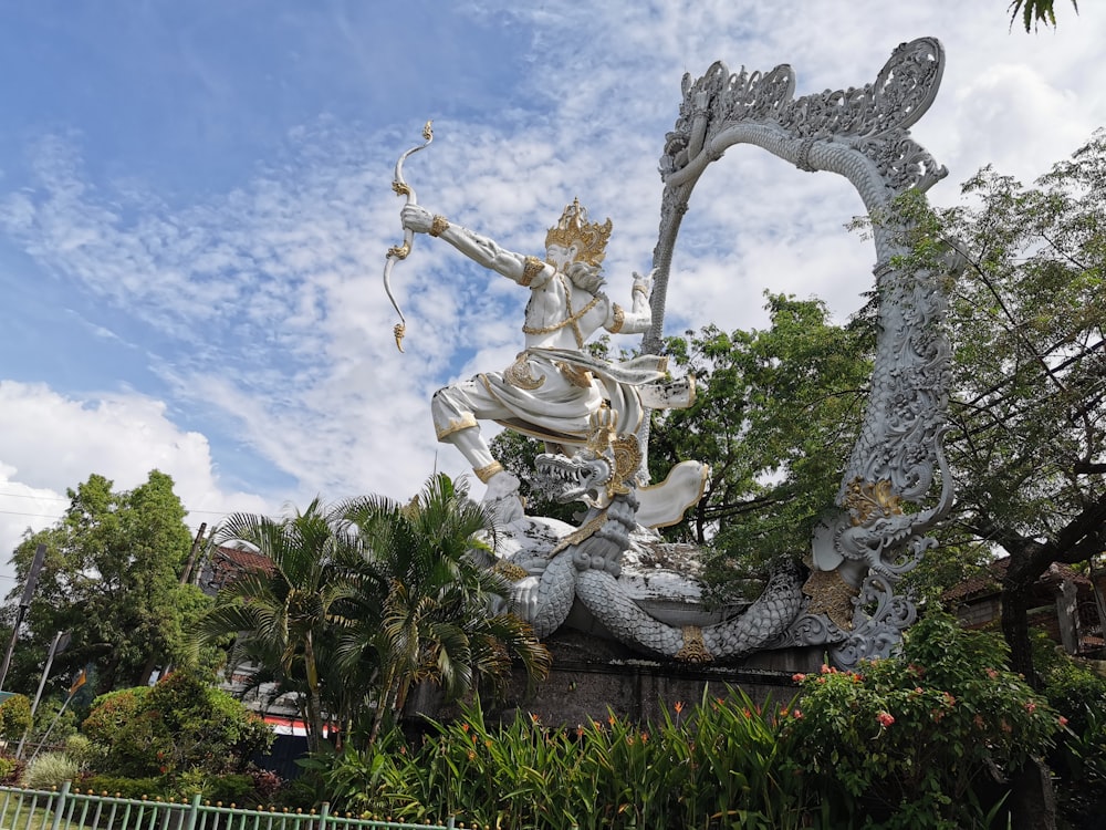 gold angel statue near green trees under blue sky during daytime