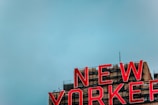 A large red neon sign spells out 'NEW YORKER' atop a building, with a clear blue sky in the background. The building has a beige facade with visible industrial elements and fixtures.