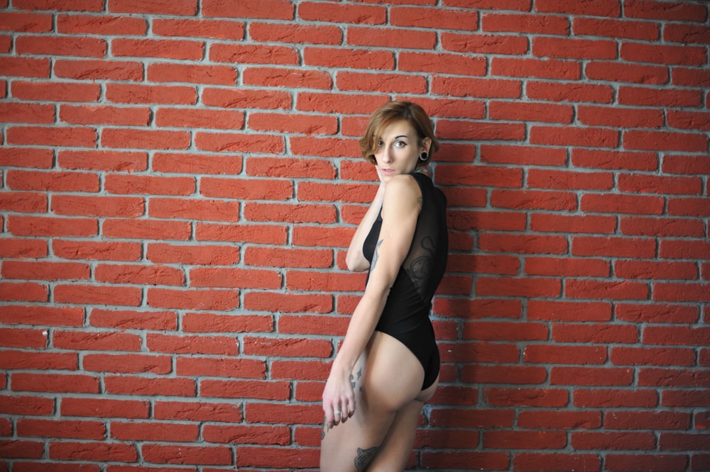 woman in black tank top leaning on red brick wall