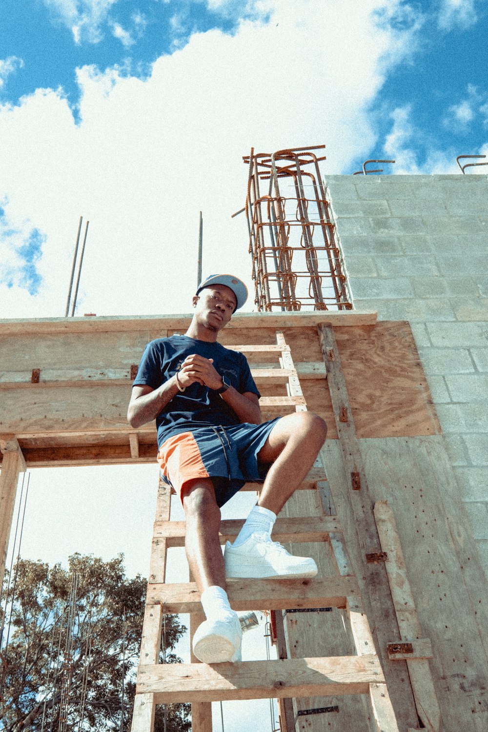 man in blue t-shirt and blue denim shorts sitting on brown concrete bench during daytime