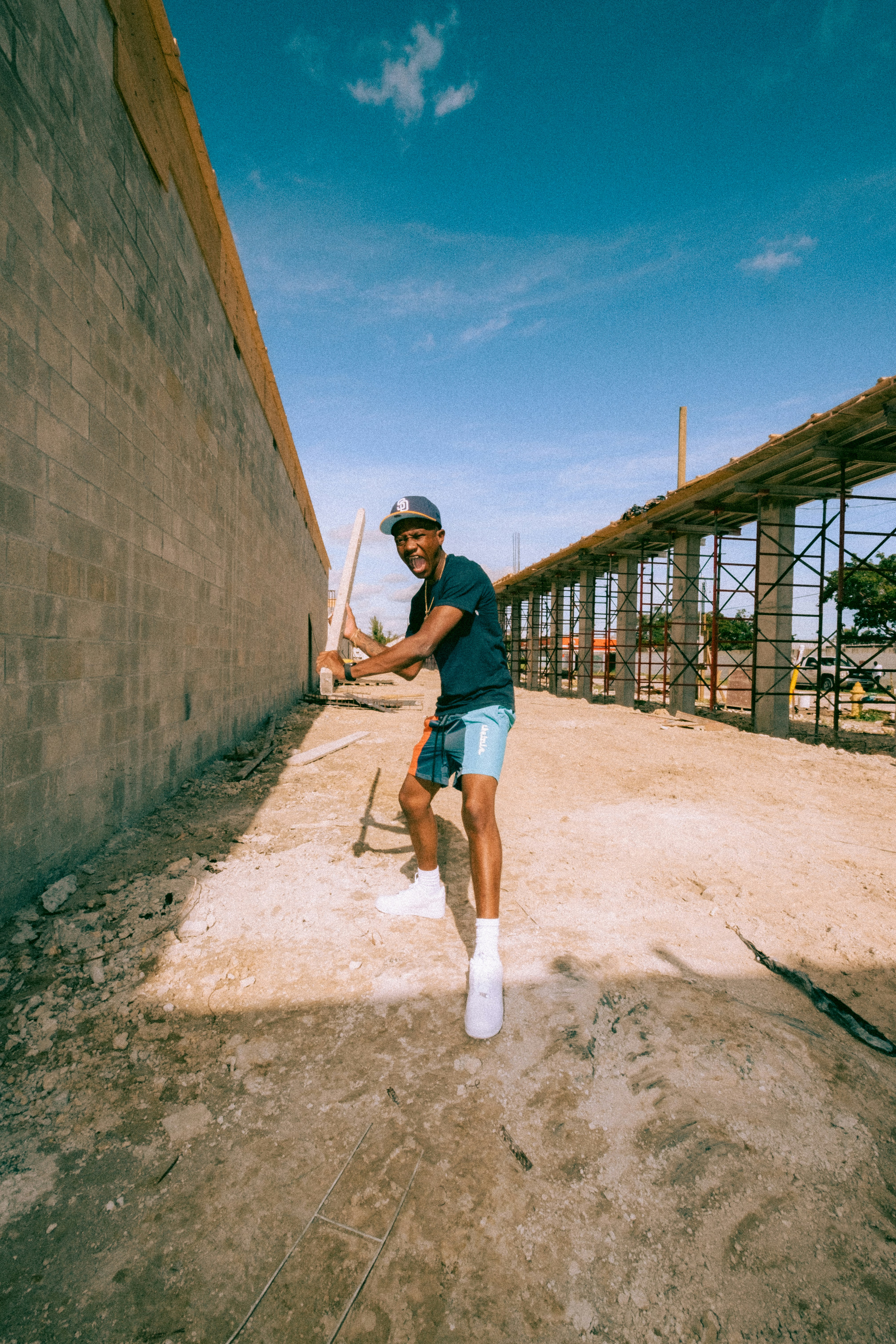 woman in blue t-shirt and white pants leaning on brown concrete wall during daytime