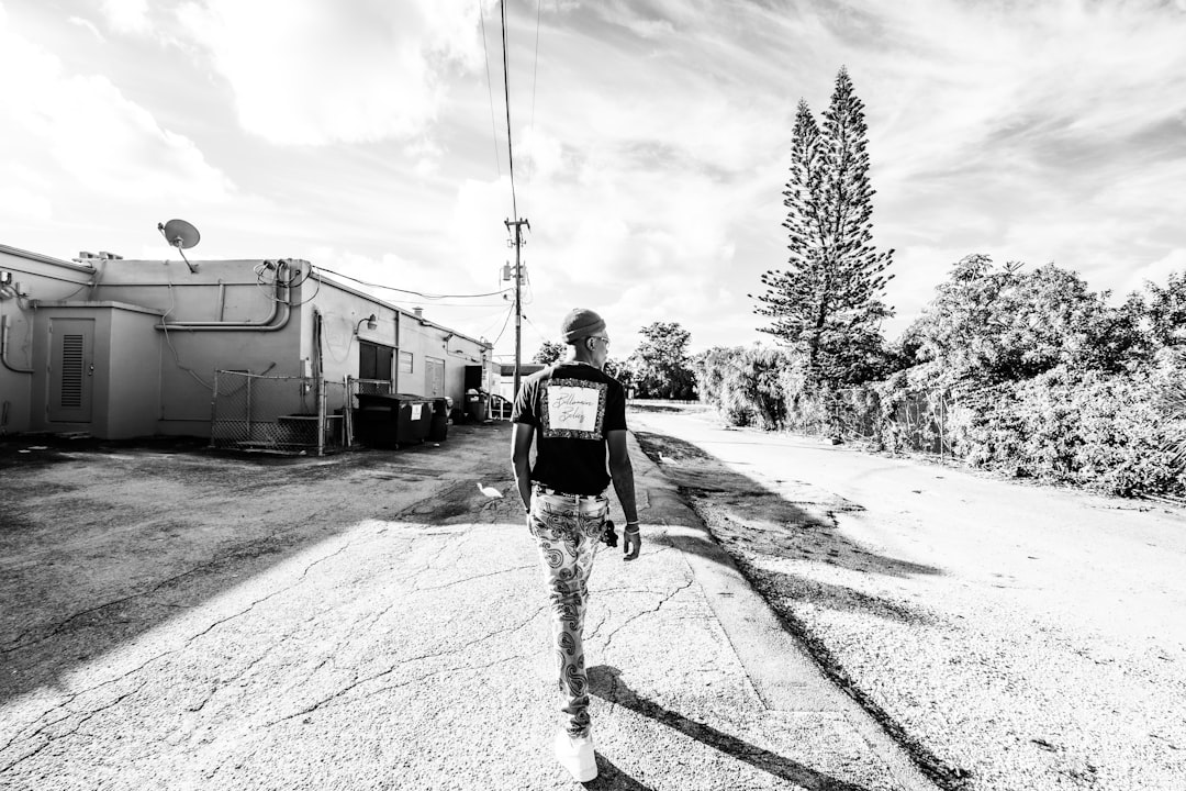 grayscale photo of man in black jacket and pants walking on road