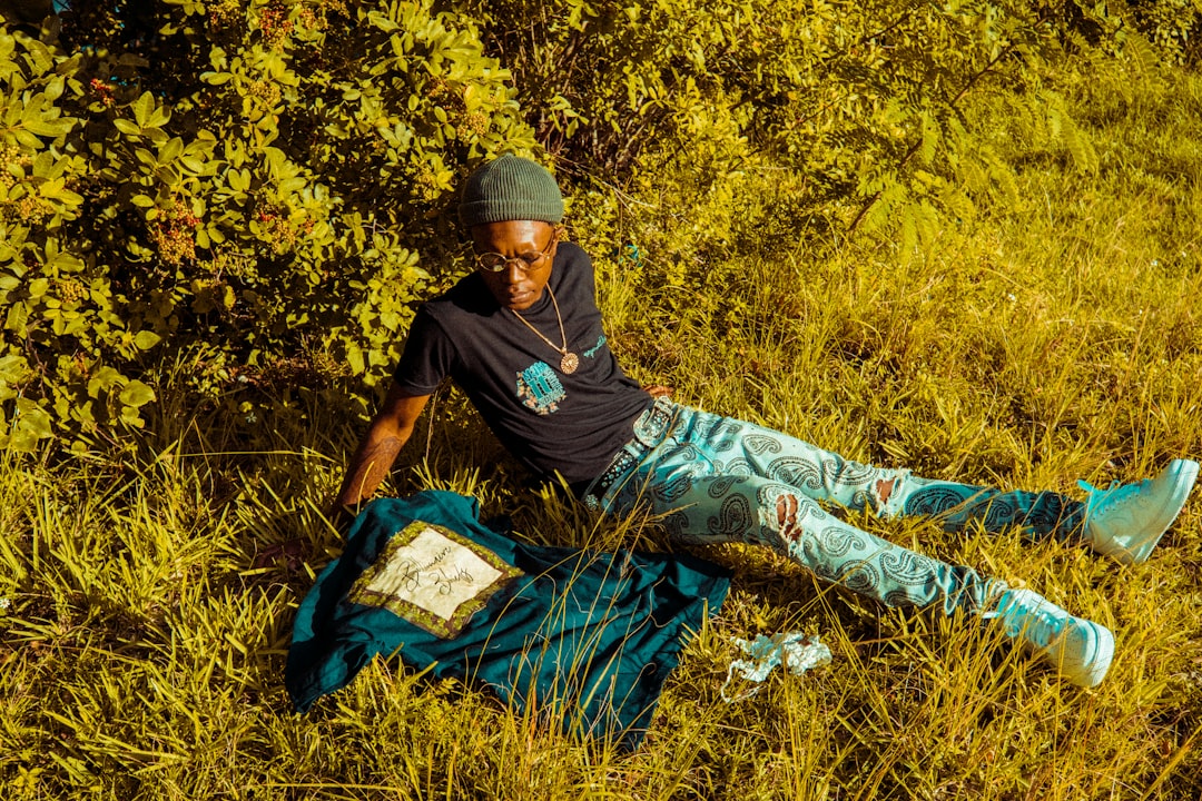 man in black long sleeve shirt and blue pants sitting on brown grass field