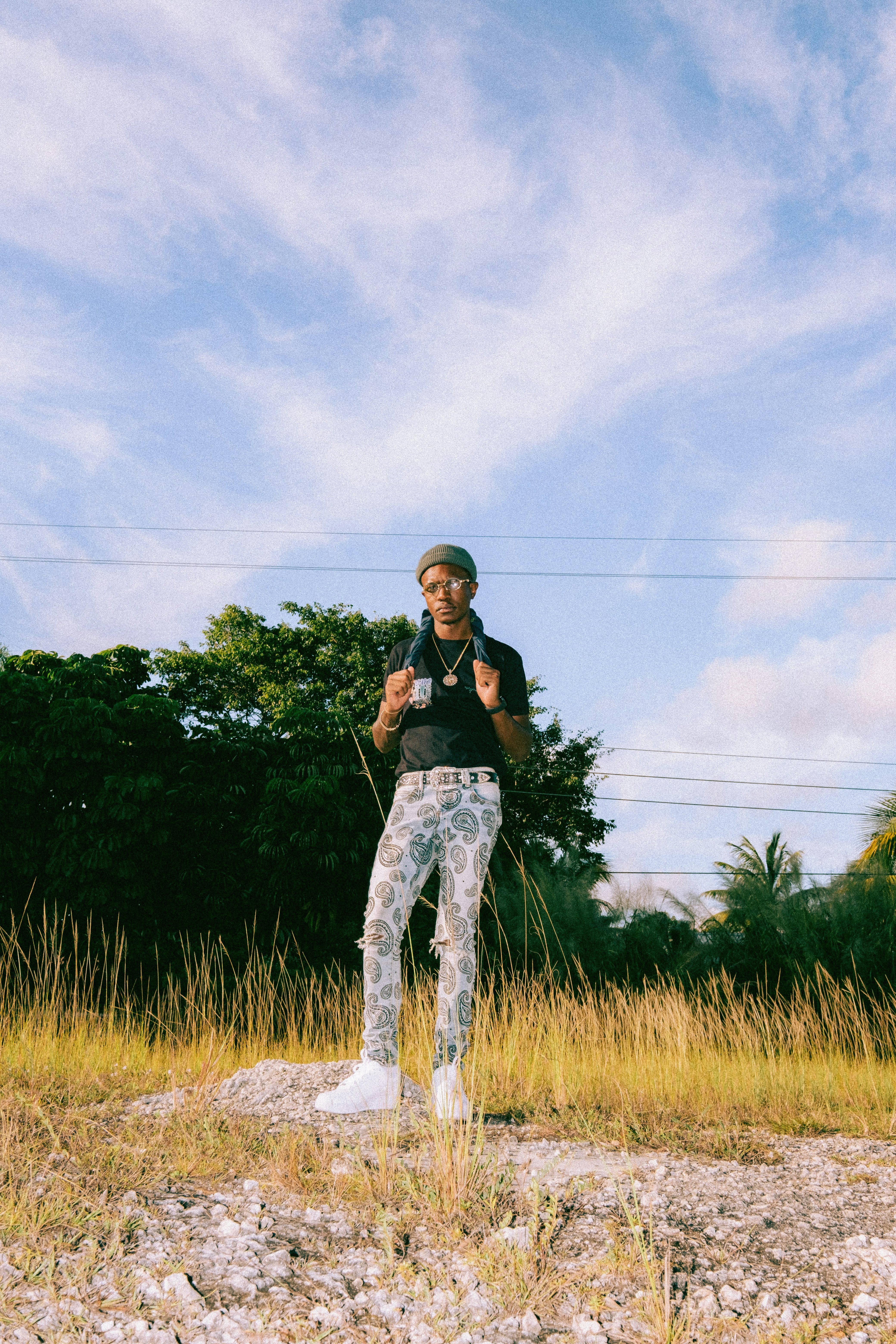 woman in black shirt and blue denim jeans standing on green grass field under white clouds