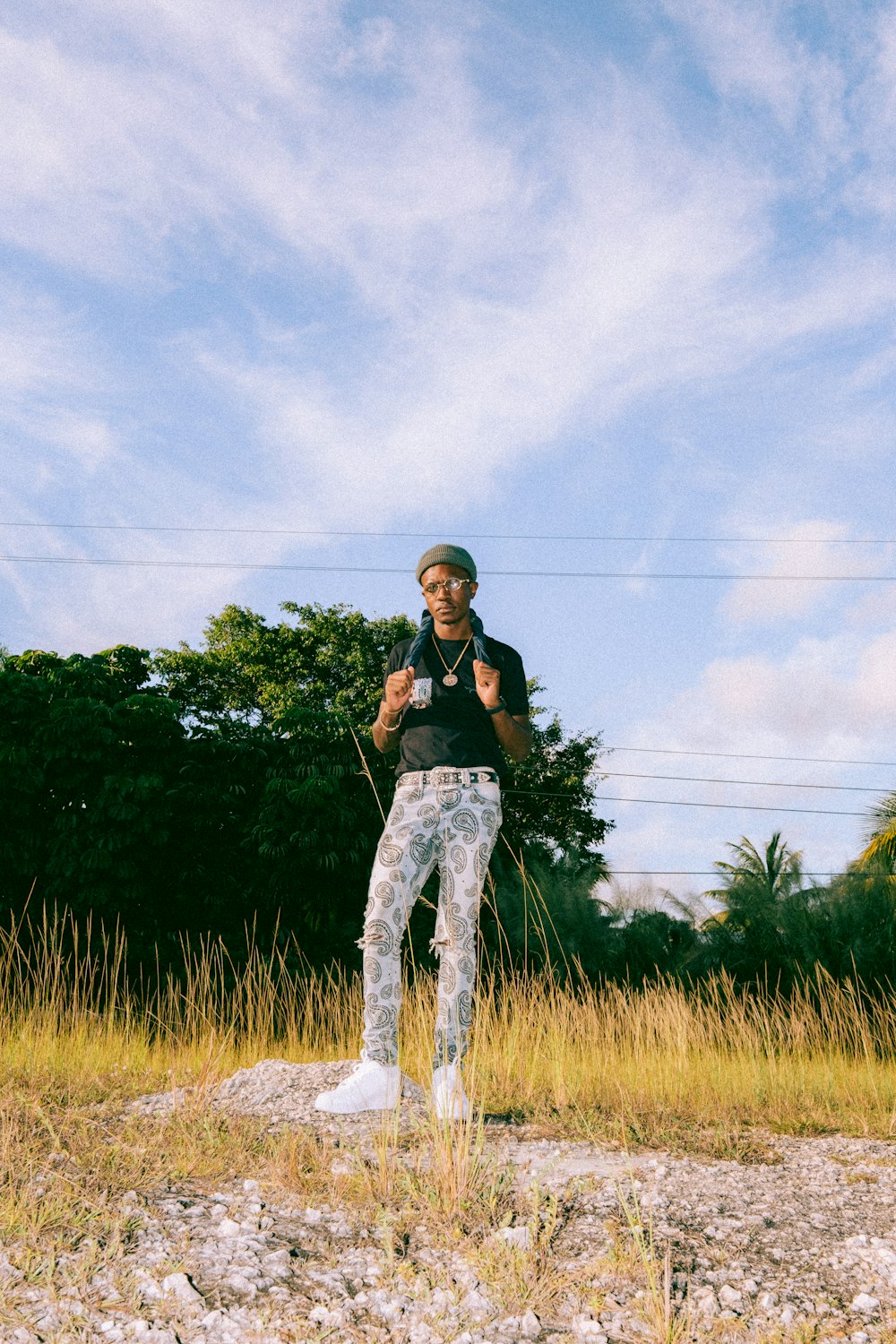 woman in black shirt and blue denim jeans standing on green grass field under white clouds