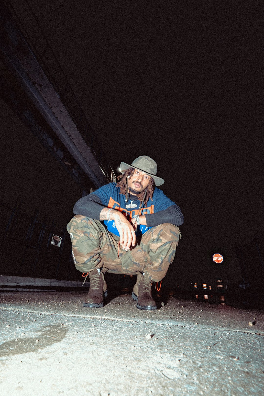 man in blue denim jacket and brown pants sitting on black asphalt road during night time