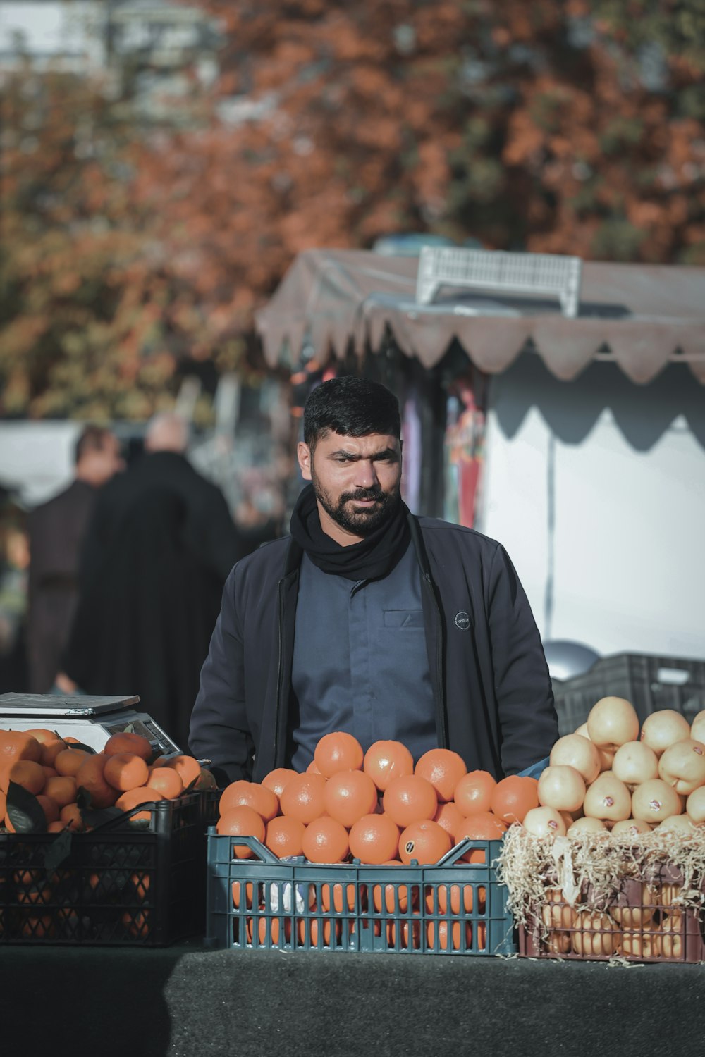 hombre en chaqueta negra de pie frente a frutas naranjas