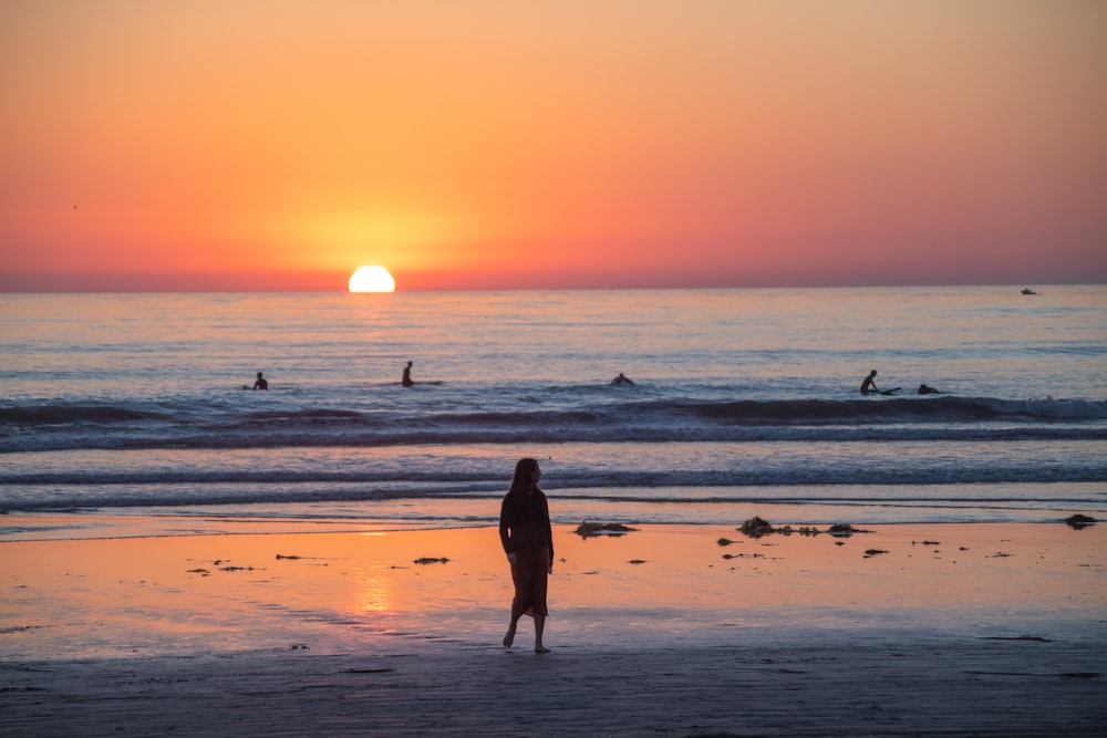mulher no vestido preto que anda na praia durante o pôr do sol
