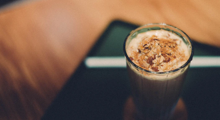 Close-up of a glass filled with creamy, spiced Banarasi thandai topped with crushed nuts and rose petals.