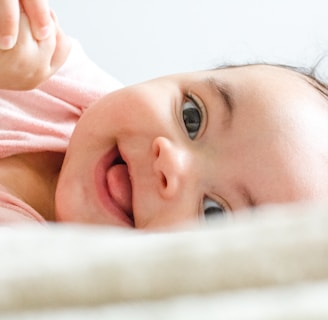 baby in pink shirt lying on white textile