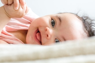 baby in pink shirt lying on white textile