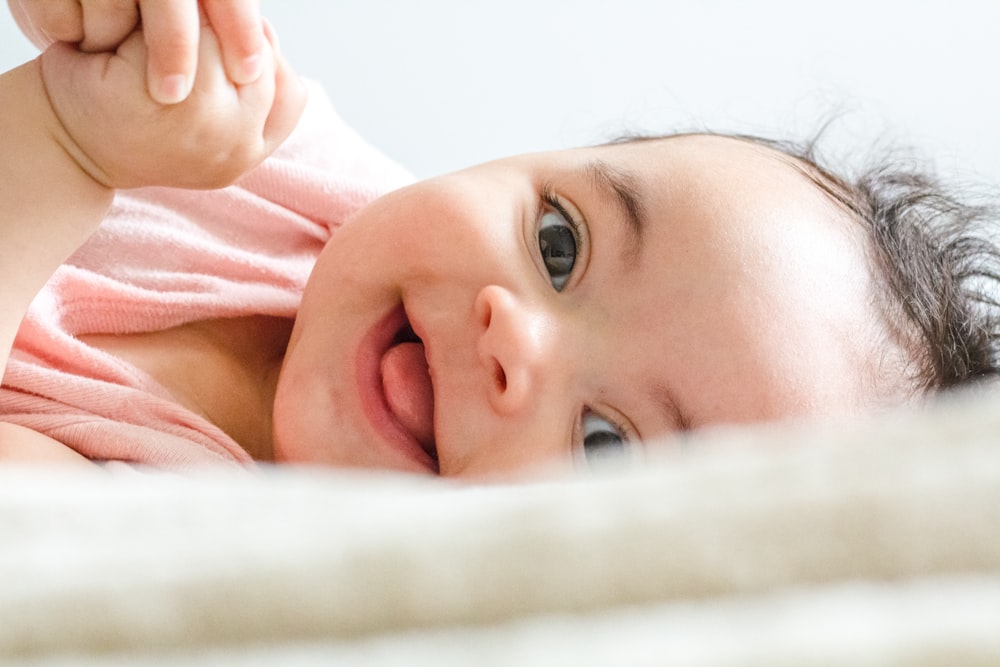 Baby im rosa Hemd liegt auf weißem Textil