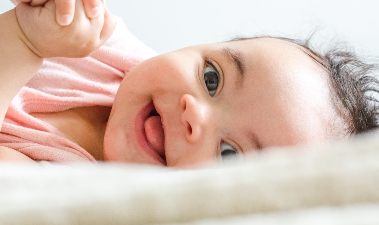 Happy baby lying on a soft blanket with hand near mouth