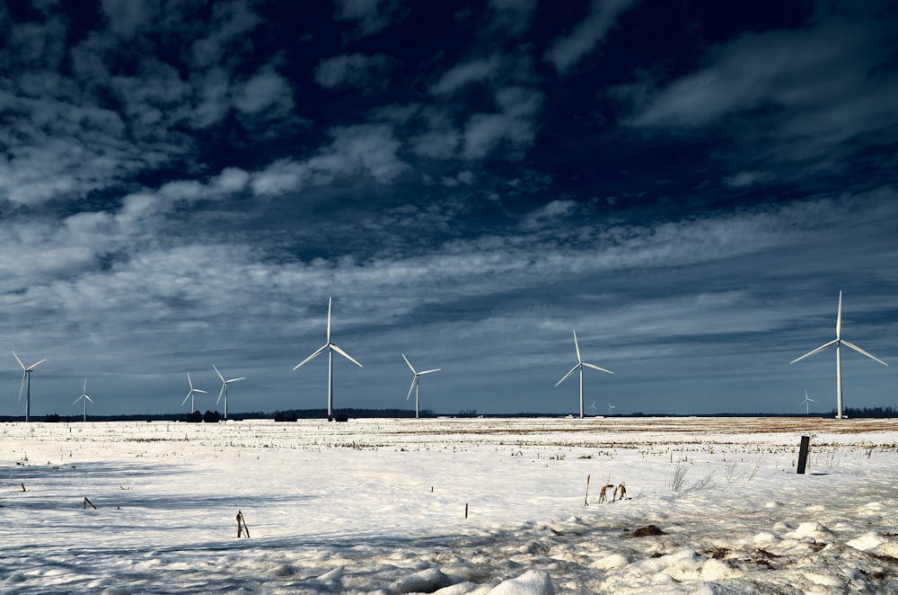 wind turbines on white snow field under blue and white cloudy sky during daytime