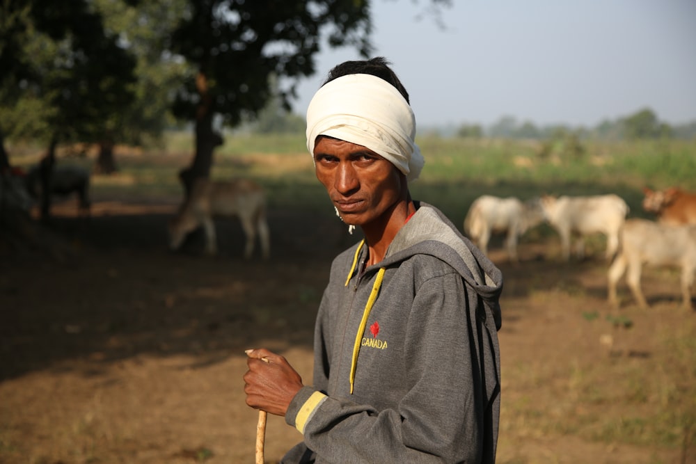 man in gray hoodie wearing white cap holding brown stick