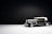 A vintage black car with a white convertible top is photographed against a minimalist dark background. The car's design reflects classic elegance, featuring chrome detailing and white wall tires. The lighting highlights the car's sleek lines and shiny surfaces, creating a dramatic effect.