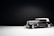 A vintage black car with a white convertible top is photographed against a minimalist dark background. The car's design reflects classic elegance, featuring chrome detailing and white wall tires. The lighting highlights the car's sleek lines and shiny surfaces, creating a dramatic effect.