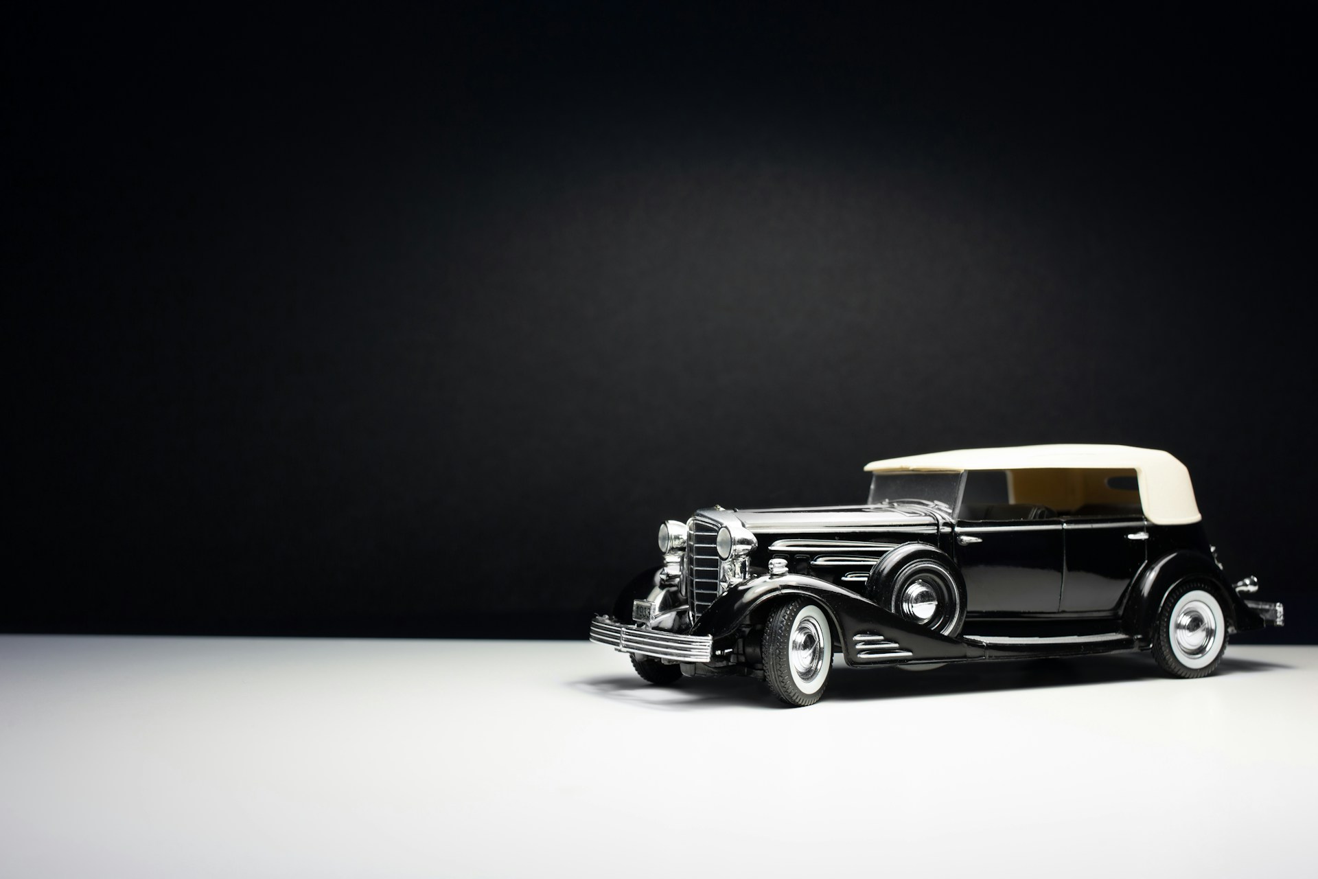 An elegant black and white photo capturing the silhouette of a vintage convertible under tall trees.