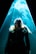 A person stands under a dramatic beam of blue light that appears to create an ethereal or mystical aura around them. The light accentuates swirling patterns, possibly smoke or mist, adding to the surreal atmosphere.