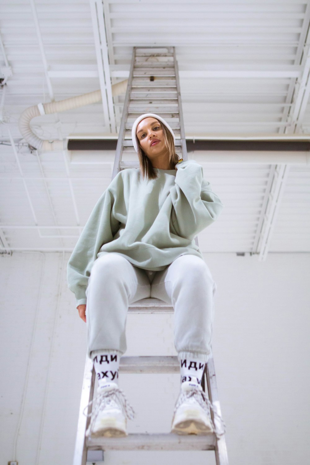 woman in green hoodie and white pants sitting on white concrete wall