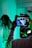 A person is being filmed with professional camera equipment in an environment illuminated by blue and green lighting. The focus is on the filming process, with the camera screen displaying the person being recorded.