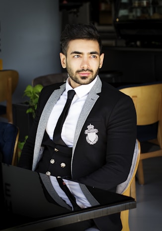 A stylish man in a classic black suit from Lumina Apparel, seated in a modern café with soft natural light.
