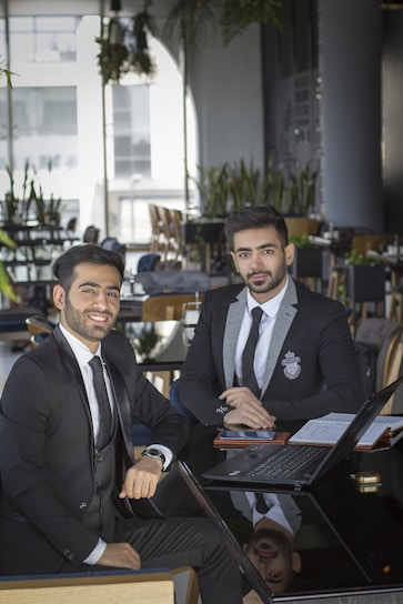 man in black suit jacket sitting beside man in black suit