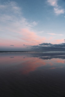 A serene travel scene with soft pink skies over a quiet beach at sunset