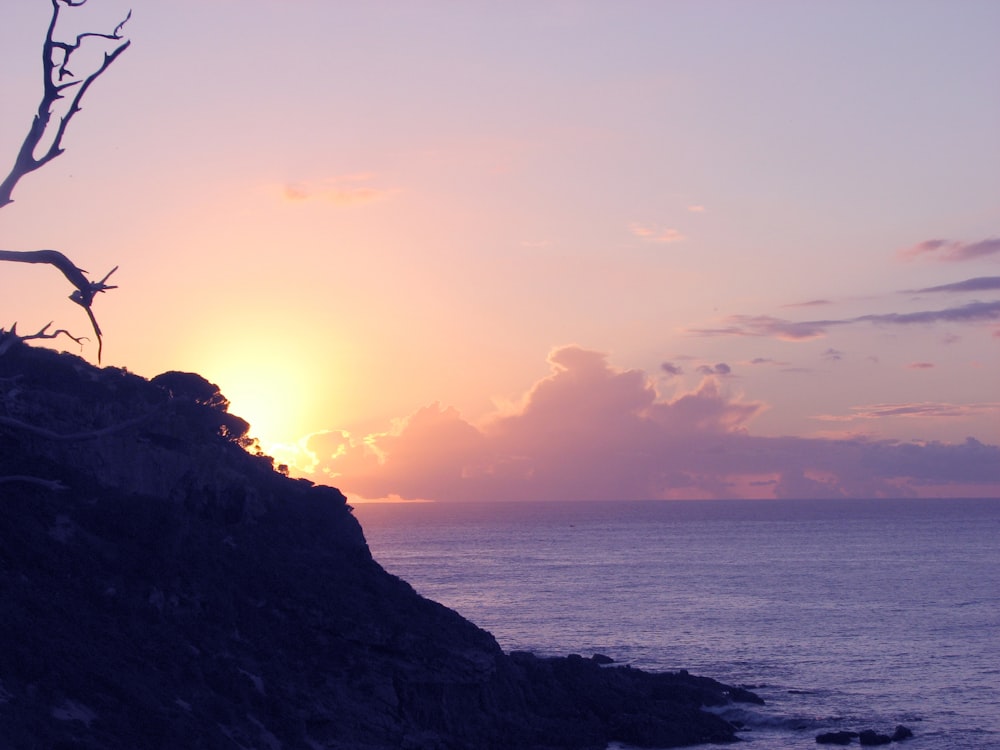 silhouette of person standing on rock formation near body of water during sunset