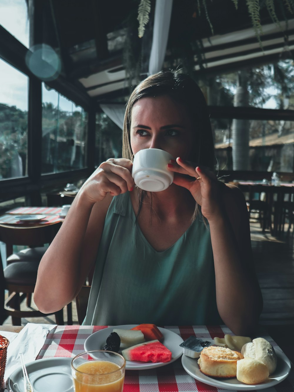 woman in teal tank top drinking from white ceramic mug