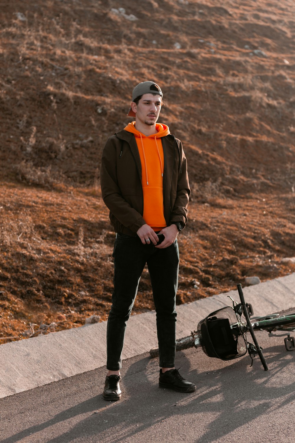 man in orange and black jacket and black pants standing on road during daytime