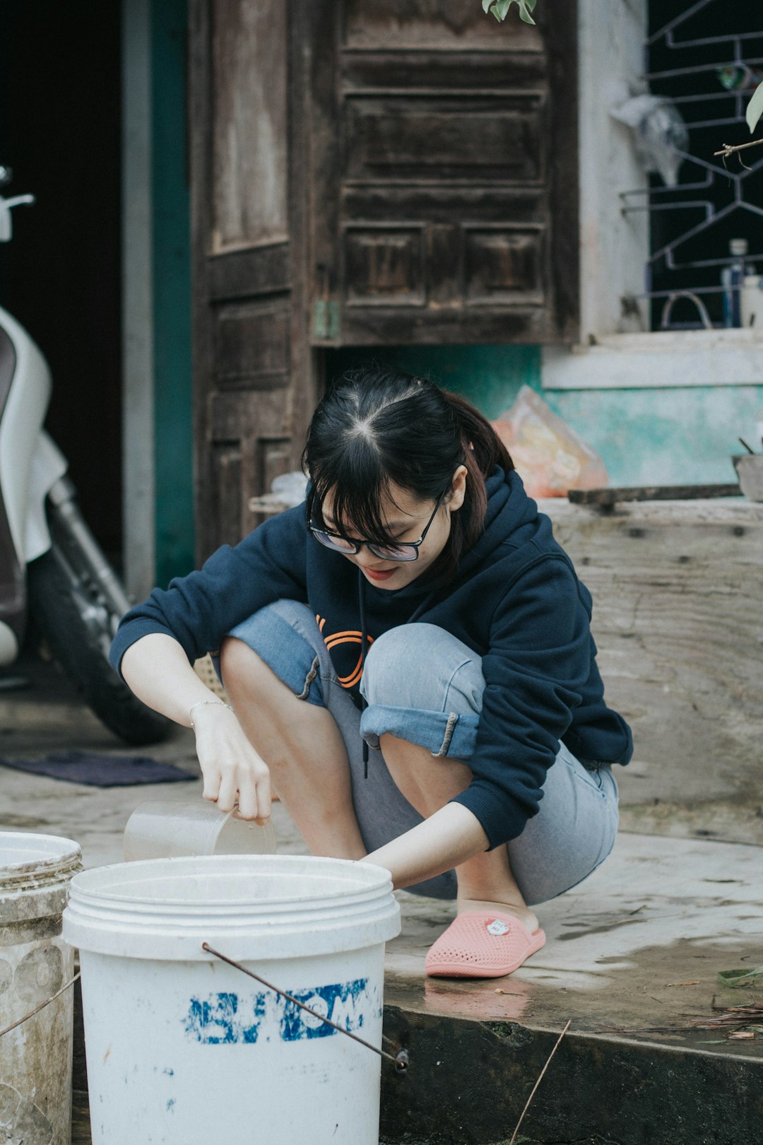 woman in black hoodie and blue denim shorts sitting on white plastic bucket