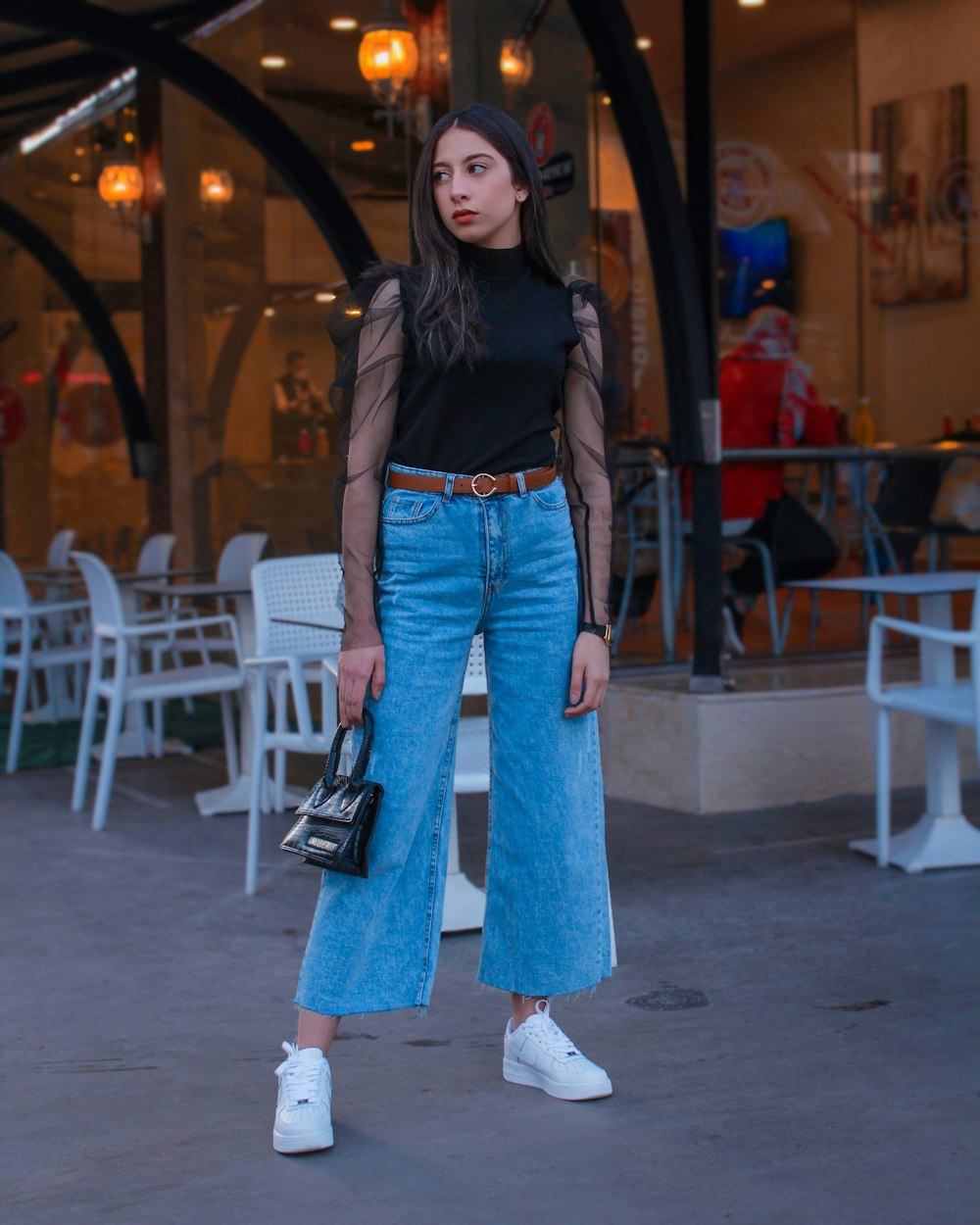 Mujer con chaqueta de cuero negra y jeans de mezclilla azul de pie sobre piso de concreto gris durante el día